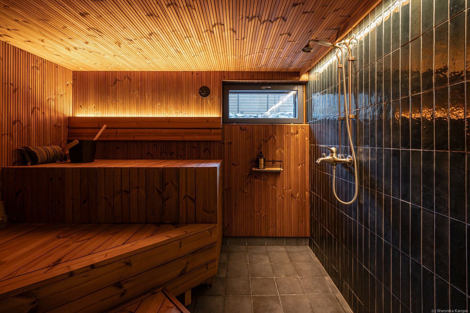 Sauna, jossa puiset lauteet, paneelikatto ja tummat seinälaatat